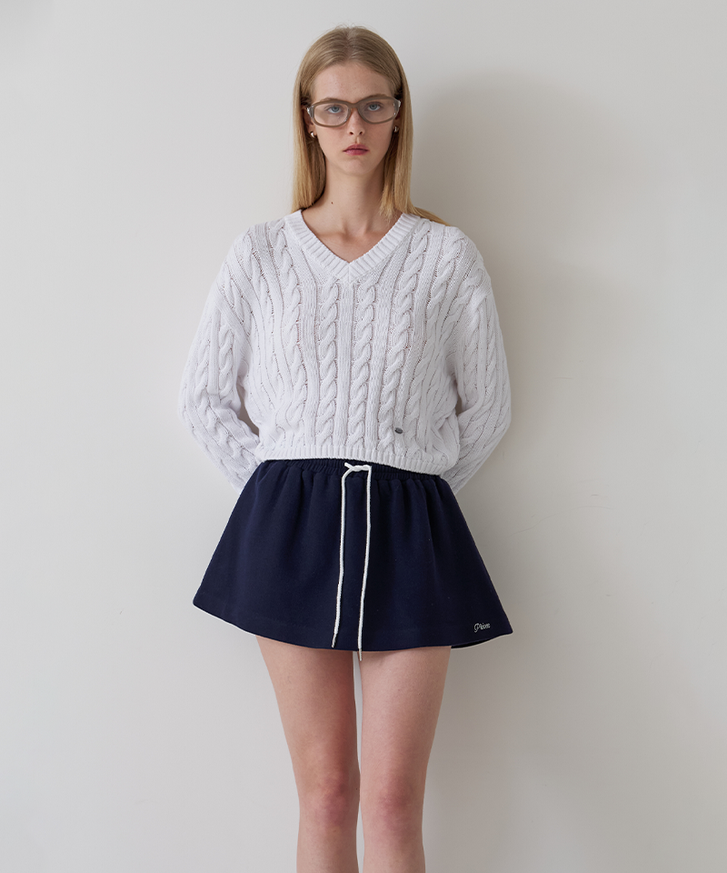 A woman wearing a white cable-knit V-neck sweater and navy blue athletic shorts with a white drawstring