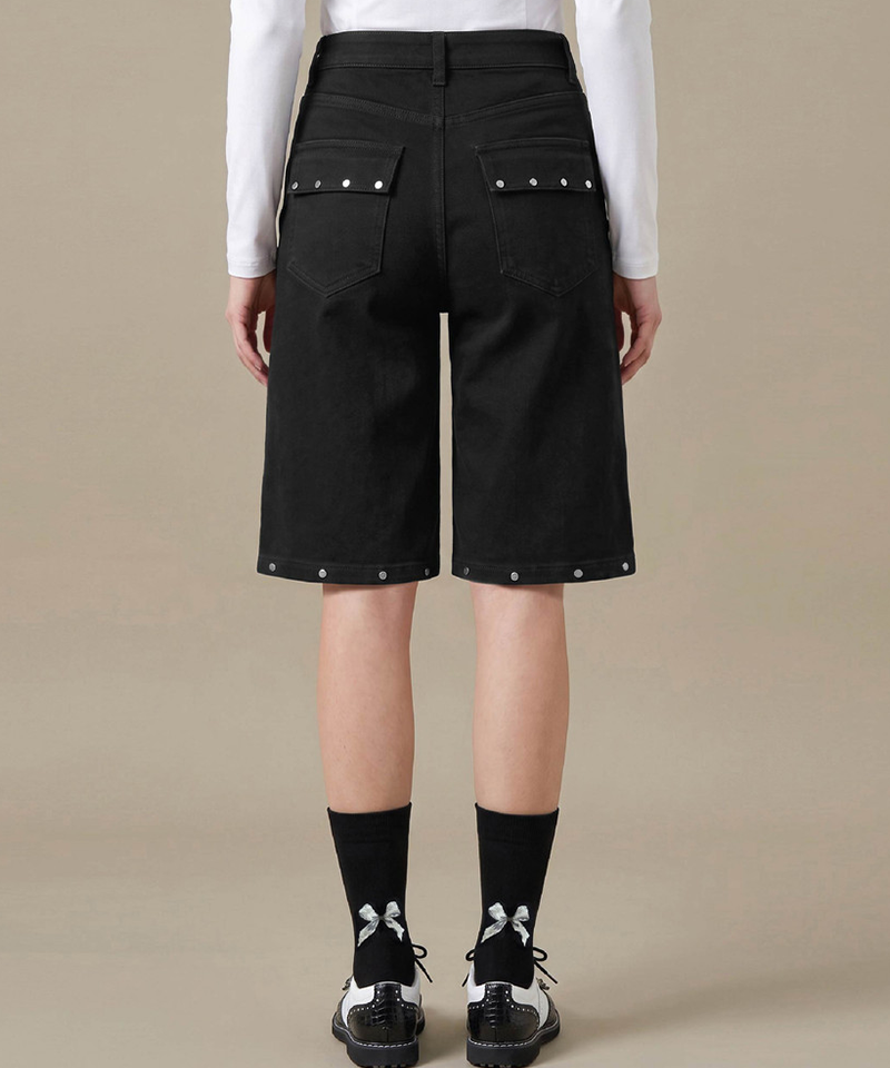 Rear view of a model wearing black denim shorts with silver rivet details on the back pockets and hem, 